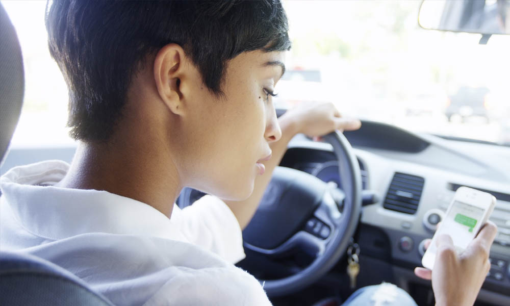 Get Serious About Distracted Driving - Woman Looking Down At Cell Phone While Sitting In Drivers Seat In Traffic