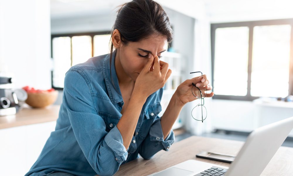 Stressed business woman working from home on laptop looking worried, tired and overwhelmed.