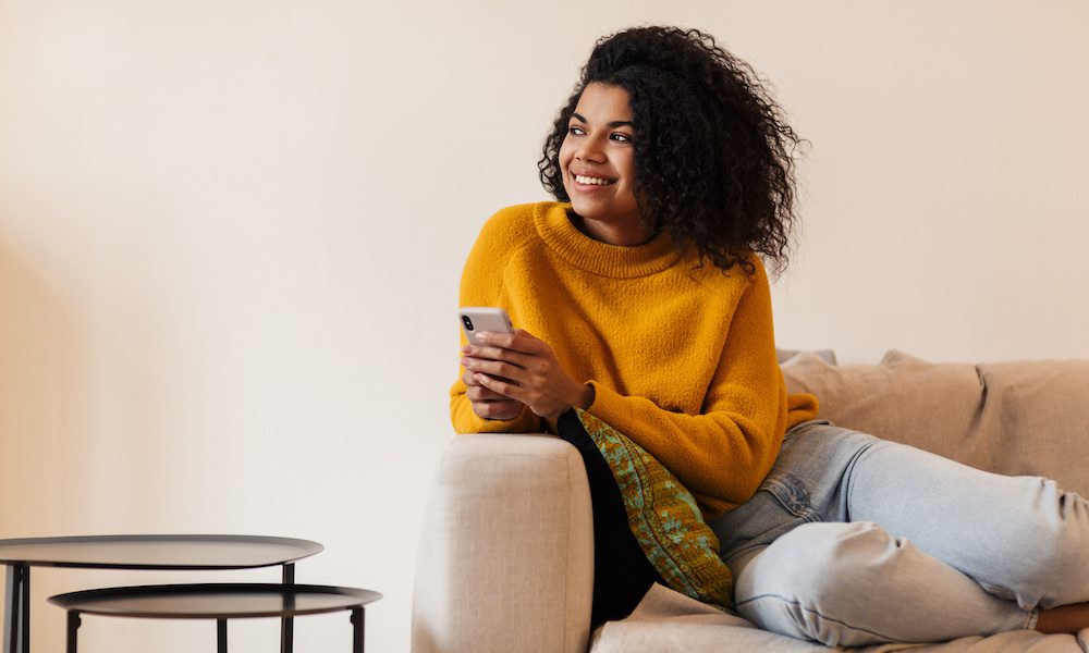Image of smiling african american woman using cellphone while sitting